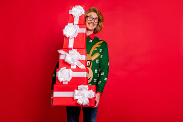 Sticker - Photo of charming sweet young man wear green sweater spectacles smiling holding many gift boxes isolated red color background