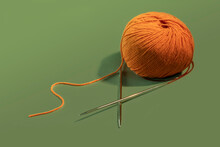 A Ball Of Orange Yarn With Knitting Needles On A Green Background. Women's Needlework