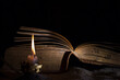 A candle burns next to an open old book. the concept of secret knowledge and mysticism. Selective focus on a candle flame.