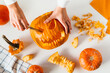Happy halloween, decoration and holidays concept. Young woman hands with knife carving pumpkin or jack-o-lantern on white table background at home. Close-up, top view, flat lay