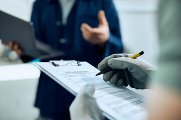 Close-up of mechanic writes notes while talks with coworker in car workshop.