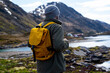Guy travels with a yellow backpack through picturesque places with beautiful mountain landscapes.