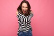 © Ivan Traimak - Young beautiful brunet woman. Trendy lady in casual striped longsleeve. Positive female shows facial sincere emotions. Funny model isolated on pink background with free space