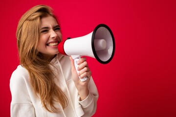 Wall Mural - Photo portrait of beautiful attractive positive happy smiling dark blonde young woman with sincere emotions wearing stylish white hoodie isolated over red background with copy space and shouting into