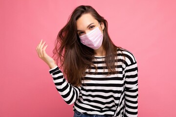 Young pretty woman in reusable virus protective pink mask on face against coronavirus isolated on the pink background wall