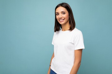 Portrait of positive cheerful fashionable smiling young brunette woman in casual white t-shirt for mockup isolated on blue background with copy space