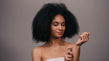 Young African American Woman Spraying Perfume On Hand Isolated On Grey