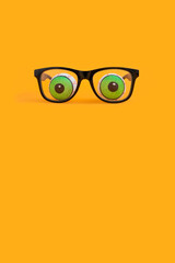 minimal funny halloween concept with eyeglasses and doll eyeballs on orange background