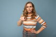 © Ivan Traimak - Portrait of angry dissatisfied young beautiful blonde curly woman with sincere emotions wearing stylish striped sweater isolated on blue background with empty space and abusing