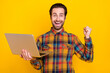 © deagreez - Photo of cute lucky young guy dressed checkered shirt holding modern gadget rising fist smiling isolated yellow color background