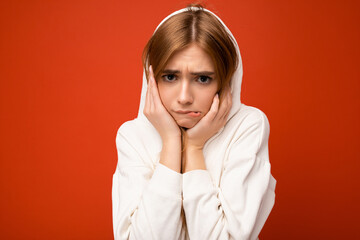 Wall Mural - Young doubtful beautiful dark blonde woman with sincere emotions isolated on background wall with copy space wearing casual white hoodie looking at camera