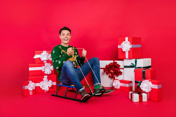 Sticker - Full length body size photo happy guy in ugly sweater smiling sitting on sledges isolated bright red color background