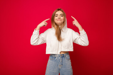 Young smiling beautiful dark blonde woman with sincere emotions isolated on background wall with copy space wearing casual white hoodie. Positive concept