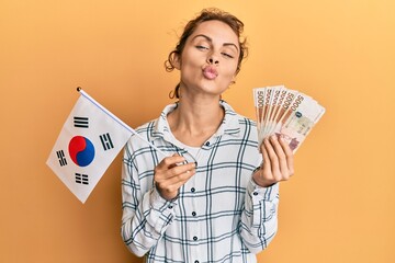 Poster - Young brunette woman holding south korean won banknotes looking at the camera blowing a kiss being lovely and sexy. love expression.