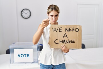 Sticker - Young blonde woman at political election holding we need a change banner pointing with finger to the camera and to you, confident gesture looking serious