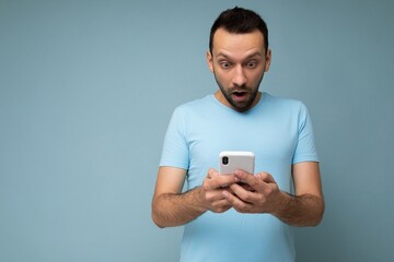 photo of shocked handsome young man with beard wearing everyday blue t-shirt isolated over blue back