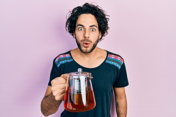 Poster - Handsome hispanic man holding traditional tea pot scared and amazed with open mouth for surprise, disbelief face