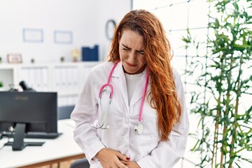 Poster - Young redhead woman wearing doctor uniform and stethoscope at the clinic with hand on stomach because nausea, painful disease feeling unwell. ache concept.