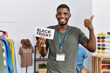 Young african american man holding black friday banner at retail shop smiling happy and positive, thumb up doing excellent and approval sign