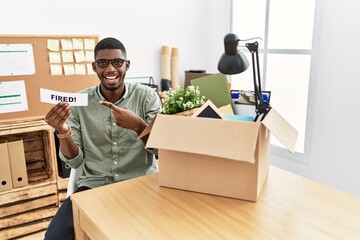 Poster - Young african american businessman holding fired banner at the office smiling happy pointing with hand and finger