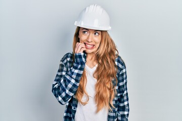 Canvas Print - Young caucasian woman wearing architect hardhat looking stressed and nervous with hands on mouth biting nails. anxiety problem.