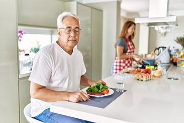 Wall Mural - Middle age hispanic couple eating healthy meal at home thinking attitude and sober expression looking self confident