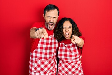 Wall Mural - Middle age couple of hispanic woman and man wearing cook apron pointing displeased and frustrated to the camera, angry and furious with you