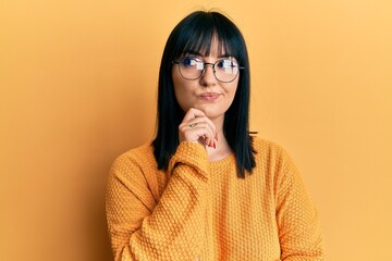 Wall Mural - Young hispanic woman wearing casual clothes and glasses thinking concentrated about doubt with finger on chin and looking up wondering