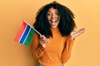 African american woman with afro hair holding gambia flag celebrating achievement with happy smile and winner expression with raised hand