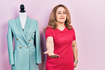 Poster - Middle age caucasian woman standing by manikin smiling cheerful offering palm hand giving assistance and acceptance.