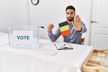 Poster - Young handsome man with beard at political campaign election holding germany flag with open hand doing stop sign with serious and confident expression, defense gesture