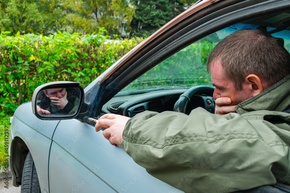 Sad and pensive driver sitting in the car in the parking lot smokes a ...