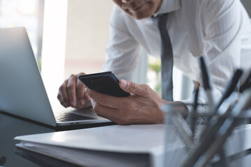 Wall Mural - Businessman using mobile smart phone working on laptop computer with business document on table in modern office