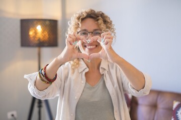 Young woman doing heart shape gesture with hands. Beautiful woman flirting and smiling on camera. Attractive cheerful woman making a heart shape symbol using her hands at home