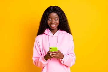 Poster - Photo portrait of african american girl holding phone in two hands isolated on vivid yellow colored background