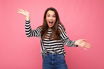 Wall Mural - Photo of young emotional astonished shocked positive happy beautiful brunette woman with sincere emotions in casual striped pullover isolated on pink background with copy space