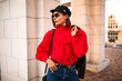 © ClaudiK - Trendy girl with stylish short hairstyle and red lips posing outside. Brunette woman in red vintage blouse and dark jacket and glasses looks away outdoors.