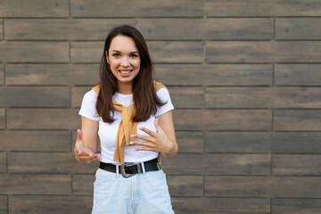 Portrait of young happy positive smiling beautiful brunette woman wearing trendy outfit standing in the street near the wall. Lifestyle concept