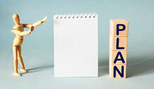 Business, Goals And Target Concept. Miniature Figure Of A Wooden Doll Next To A Notepad And Wooden Blocks With The Text PLAN