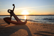 Wooden Anchor On Shore Near River At Sunset