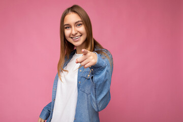 Wall Mural - Photo of young positive happy smiling beautiful woman with sincere emotions wearing stylish clothes isolated over background with copy space and pointing at camera