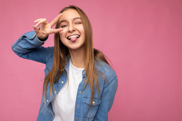 Wall Mural - Portrait of positive happy young attractive dark blonde woman with sincere emotions wearing blue jean shirt and white t-shirt for mockup isolated over pink background with empty space and having fun