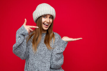 Wall Mural - Photo of young positive happy smiling beautiful woman with sincere emotions wearing stylish clothes isolated over background with copy space and pointing at free space