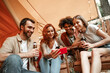 © Marharyta Hanhalo - Happy group of young people drinking wine beer using phones social media during picnic in forest smiling millennial users customers talking shopping online sit at table, mobile tech lifestyle concept