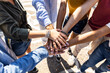 © Xavier Lorenzo - High angle view of multiracial friends stacking hands - Group of young college students work team celebrating together outdoors - Community, teamwork, unity and friendship concept