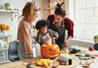 © JenkoAtaman - Happy african american family mother, father and child son carving pumpkin for Halloween holiday together at home