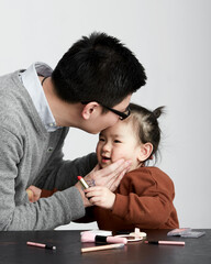 Wall Mural - Asian little girl and parents playing makeup game, indoor white background