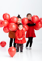 Wall Mural - Cute Asian little sisters are playing with red festive balloons indoors with white background