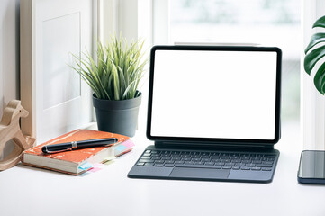 Blank screen tablet with magic keyboard on white table in living room, home office concept.