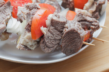  raw goat meat with chopped tomatoes and onions on skewers on a wooden board close-up